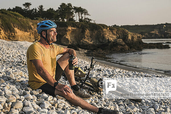 Thoughtful mature man sitting with bicycle on pebbles