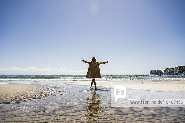 Frau mit ausgestreckten Armen läuft an einem sonnigen Tag im Wasser am Strand