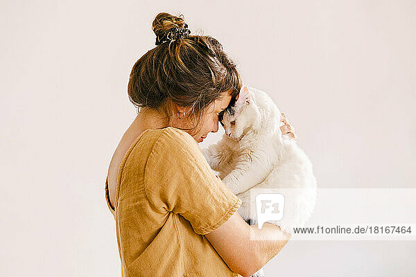 Woman playing with cat in front of wall at home