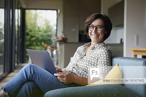 Happy woman with laptop sitting on sofa at home