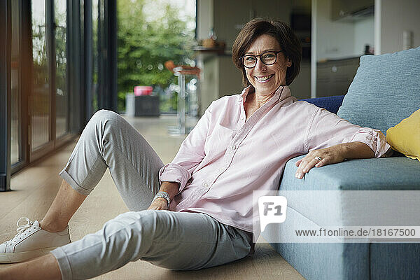 Happy woman sitting on floor by sofa at home