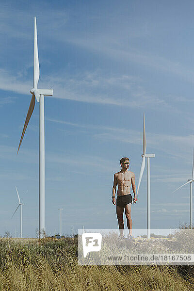 Shirtless young athlete in front of wind turbine