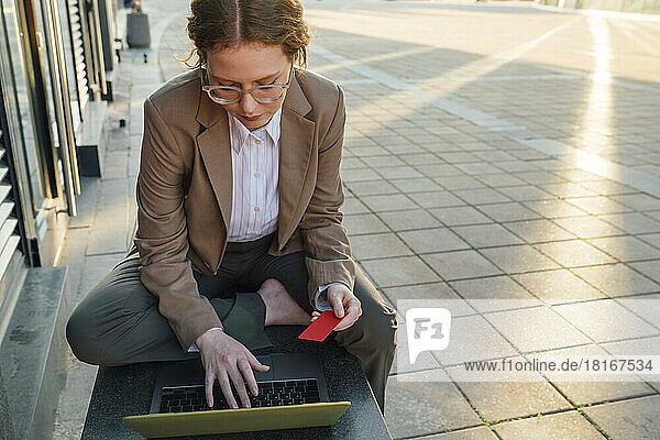 Junge rothaarige Geschäftsfrau bezahlt online per Kreditkarte mit Laptop