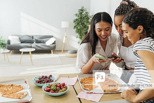 Lächelnde Freunde  die Smartphones in der Küche benutzen