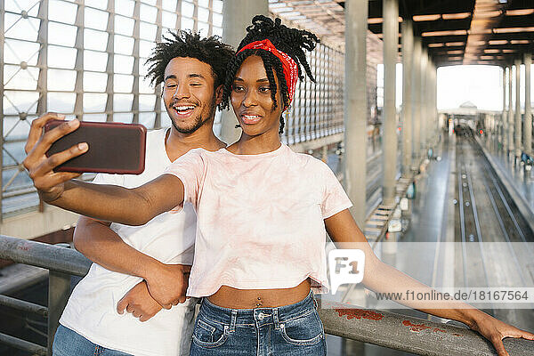 Smile young man and woman taking selfie on smart phone at railroad station