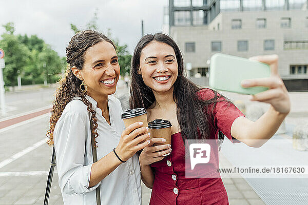 Smiling woman taking selfie with friend on smart phone