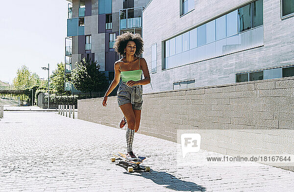 Young woman longboard skating outside building on sunny day