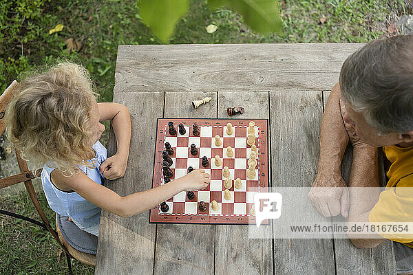 Enkelin und Großvater spielen Schachbrett im Garten