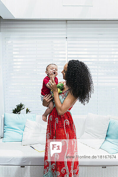Happy mother with baby boy standing in front of sofa at home