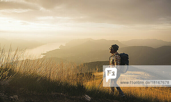 Man with hiking pole and backpack hiking at sunrise
