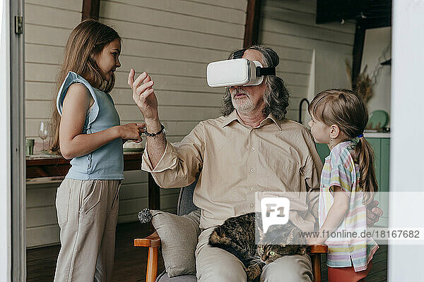 Grandfather wearing virtual reality simulator gesturing by grandchildren at home
