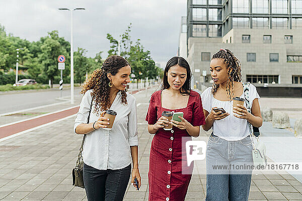 Young woman sharing smart phone with friends walking on footpath