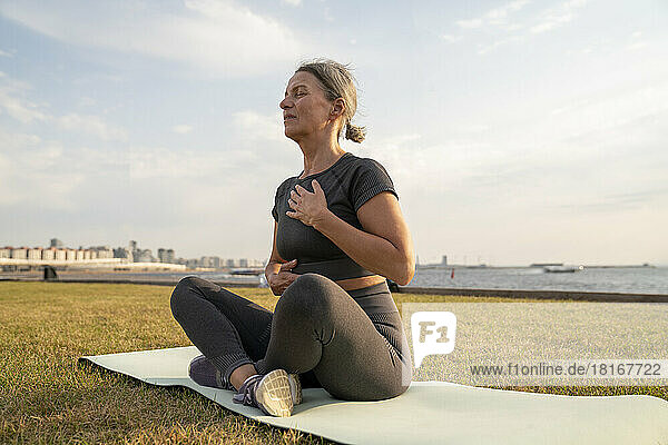 Mature woman practicing yoga on grass at sunset