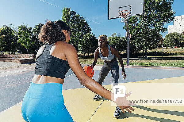 Young sportswoman dribbling basketball playing with friend in sports court