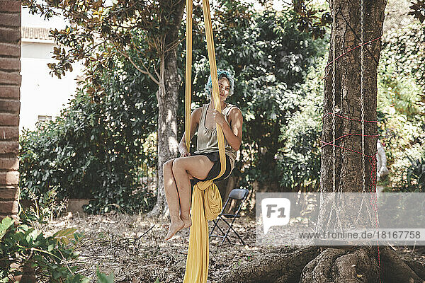 Frau hängt an Luftseide und praktiziert Acroyoga am Baum