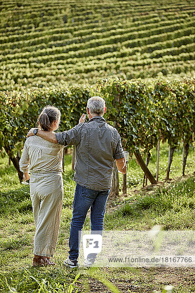 Man and woman holding wineglasses in front of vineyard