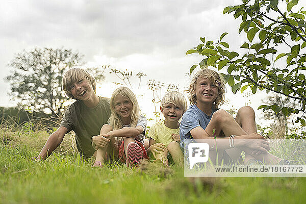 Smiling brothers and sister with blond hairs sitting on grass