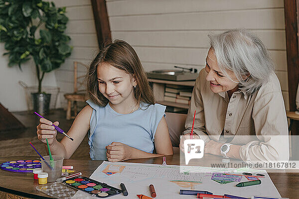 Grandmother helping granddaughter in painting at home