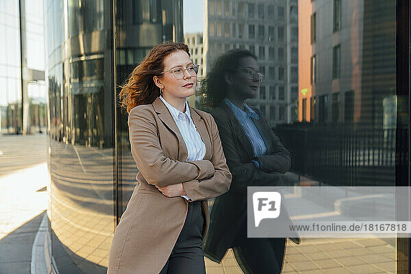 Thoughtful businesswoman leaning on office building with reflection