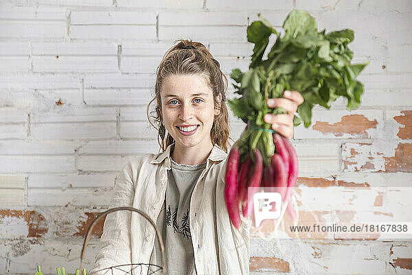 Smiling owner showing fresh radish in front of brick wall