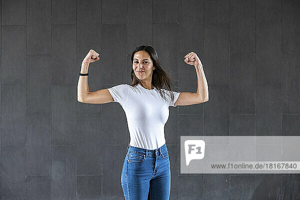 Happy woman flexing muscles in front of gray wall