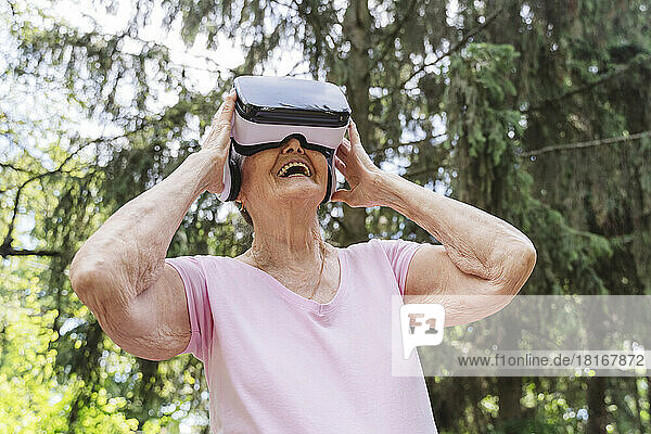 Glückliche ältere Frau schaut durch VR-Brille im Park zu