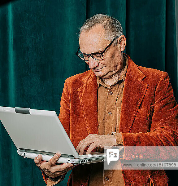 Älterer Mann benutzt Laptop vor Vorhang