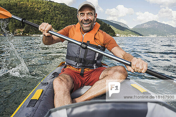 Happy man in life jacket rowing kayak boat at lake