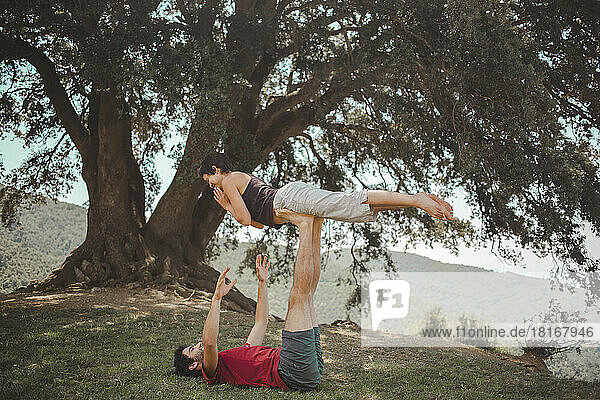 Young couple practicing acroyoga under oak tree