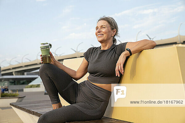 Happy woman holding water bottle on bench