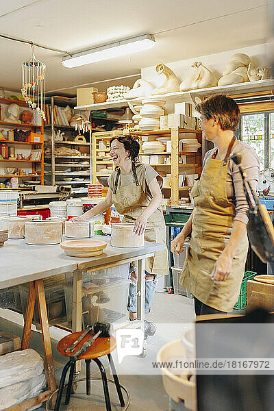 Cheerful potter with colleague working at ceramics workshop