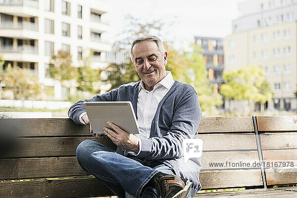 Smiling senior man using tablet PC sitting on bench