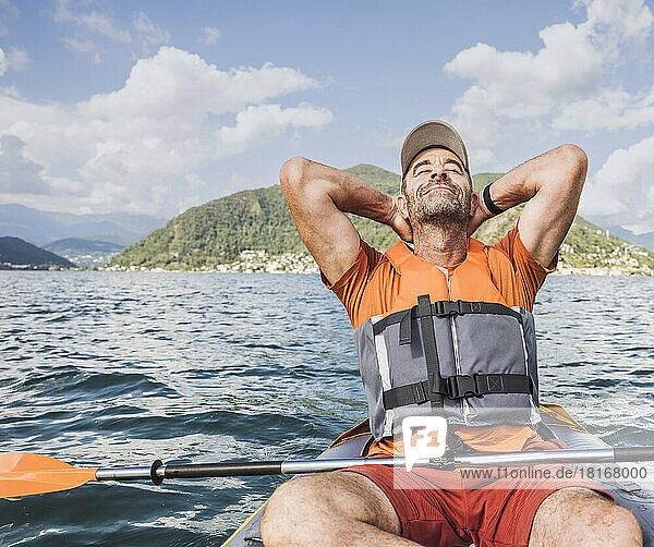 Reifer Mann entspannt sich mit den Händen hinter dem Kopf im Kajak auf dem See