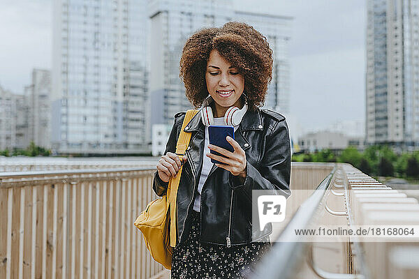Smiling woman text messaging through smart phone standing by railing