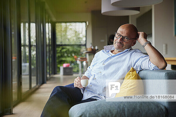 Retired senior man with coffee cup sitting on sofa at home