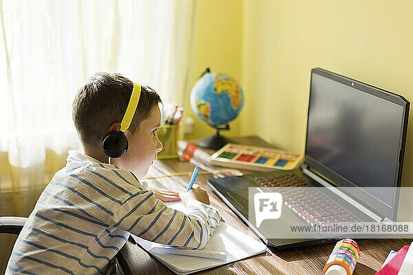 Boy wearing headphones using laptop at home