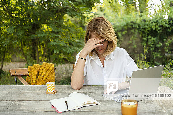 Stressed freelancer sitting with laptop at table in garden