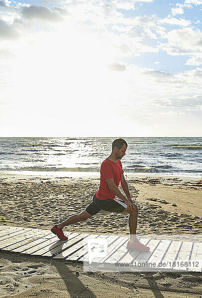 Man doing stretching exercise on boardwalk at beach