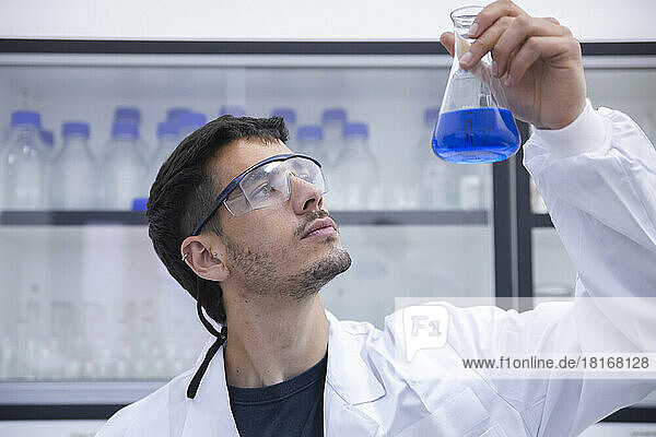 Wissenschaftler mit Schutzbrille untersuchen blaue Chemikalie im Kolben im Labor