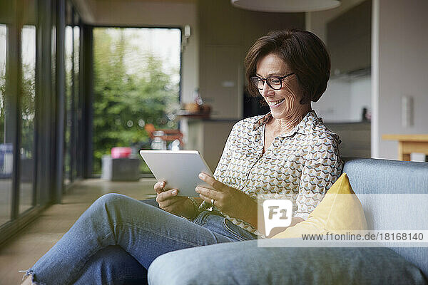 Happy senior woman using tablet PC on sofa at home