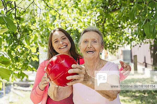 Cheerful fitness instructor teaching exercise with ball to senior woman at park