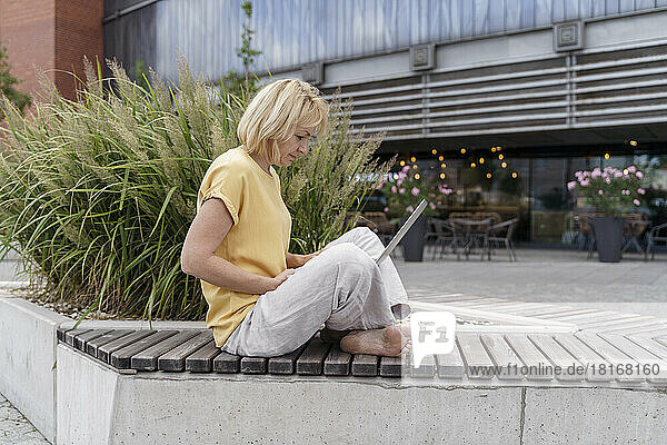 Mature blond freelancer using laptop on bench