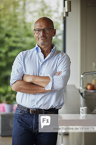 Senior man with arms crossed standing by kitchen island at home