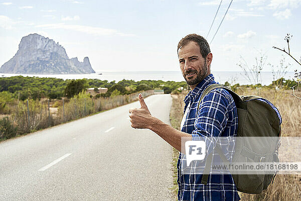 Smiling man wearing backpack gesturing thumbs up on road