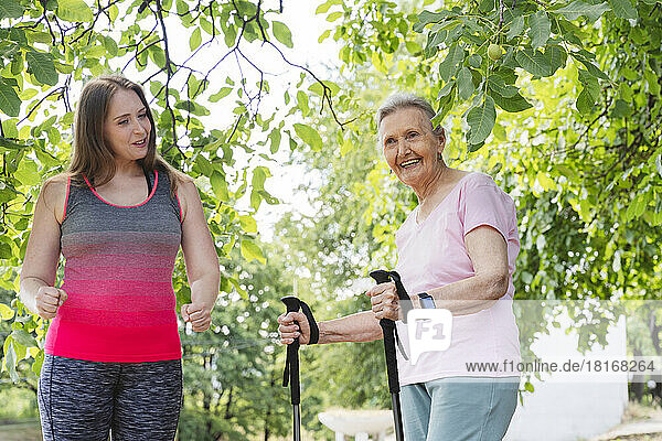 Fitness instructor teaching exercise to senior woman with walking pole in park