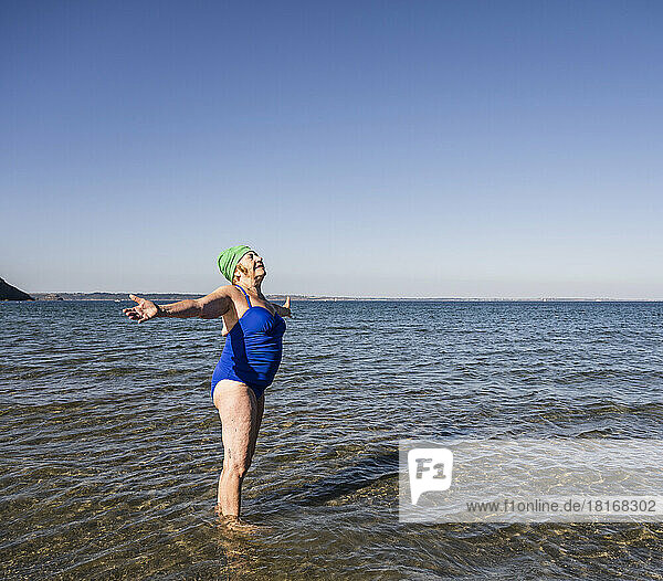 Senior woman with arms outstretched amidst sea at beach