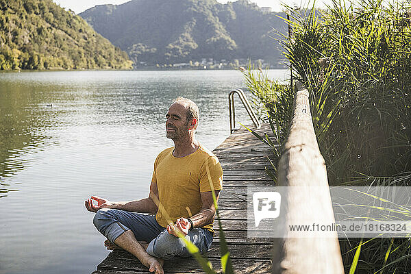 Mature man practicing lotus position on jetty by lake