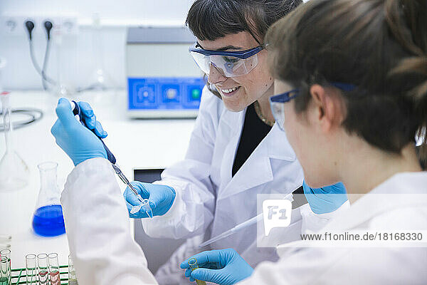 Smiling scientist using pipette for experimenting with coworker in laboratory