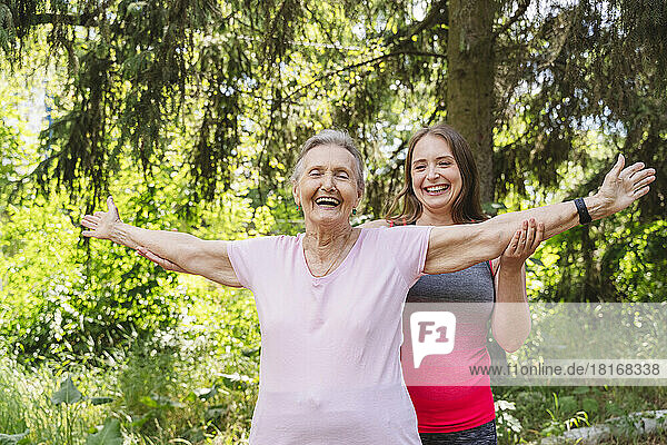 Cheerful senior woman with fitness instructor practicing stretching exercise at park