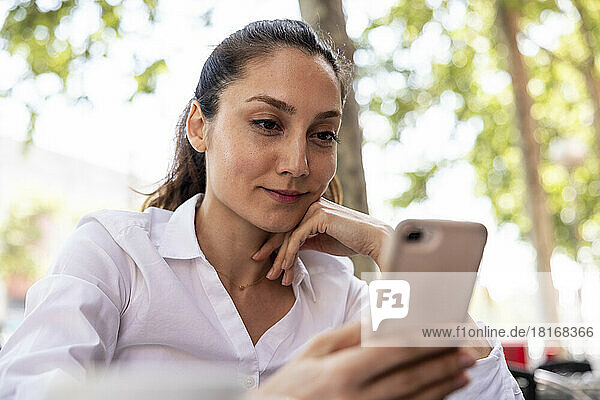 Smiling freelancer using smart phone at sidewalk cafe
